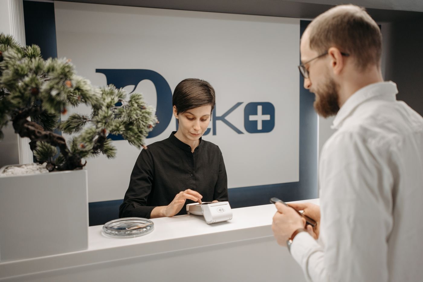 A clinic receptionist taking a card payment from a patient at the front desk